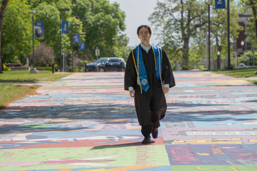 Graduate walking across campus in graduation regalia